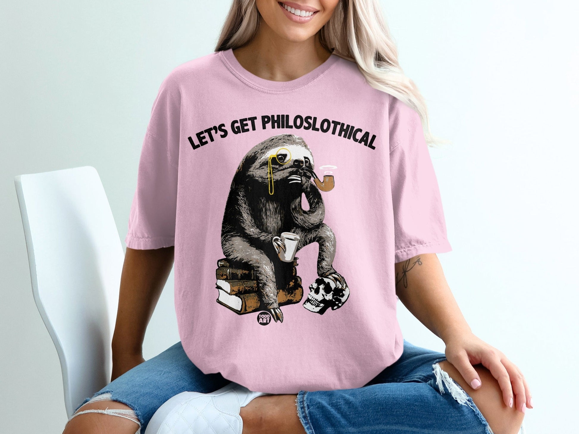Pink t-shirt with a sloth wearing a monocle smoking a pipe on books with a skull.