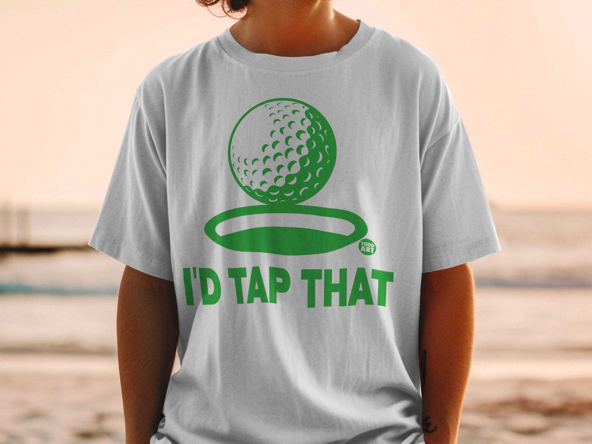 White t-shirt with green golf ball graphic and "I'd Tap That" text.