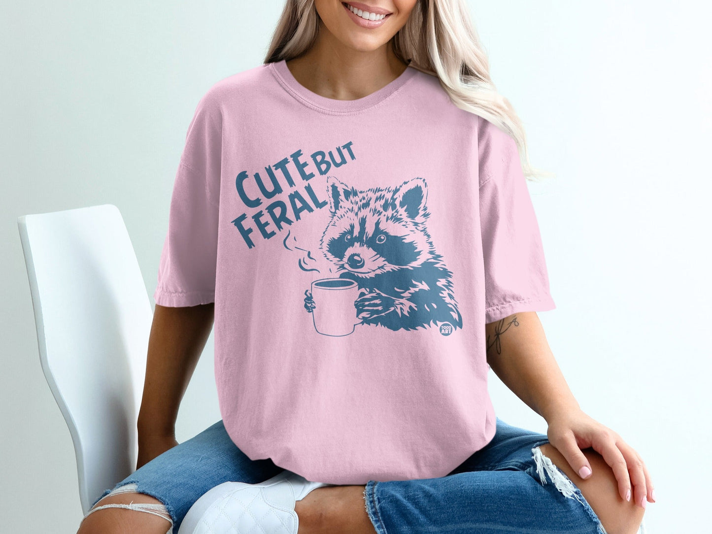 Pink t-shirt with text "CUTE BUT FERAL" and raccoon holding a coffee cup.