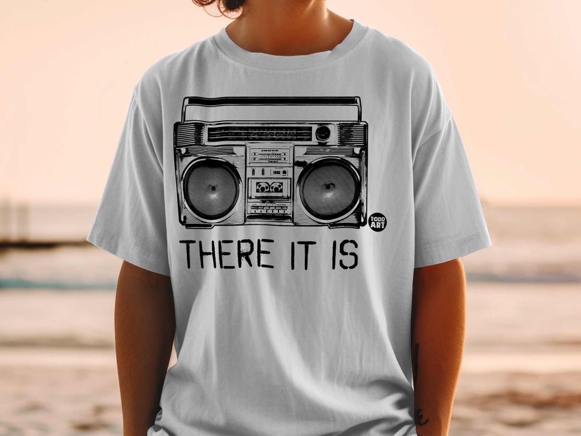 White t-shirt with a black graphic of a boombox and text "THERE IT IS".