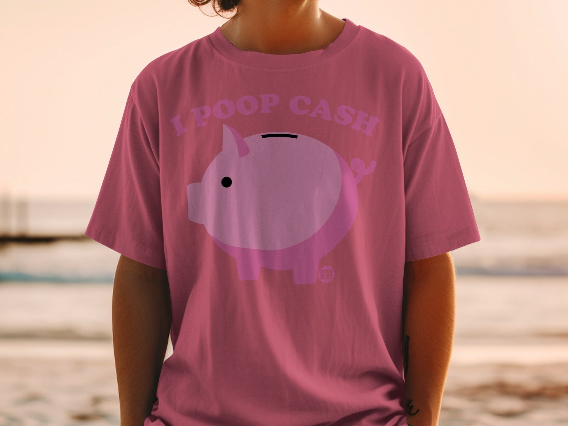 Pink t-shirt with a piggy bank graphic and text "I POOP CASH".
