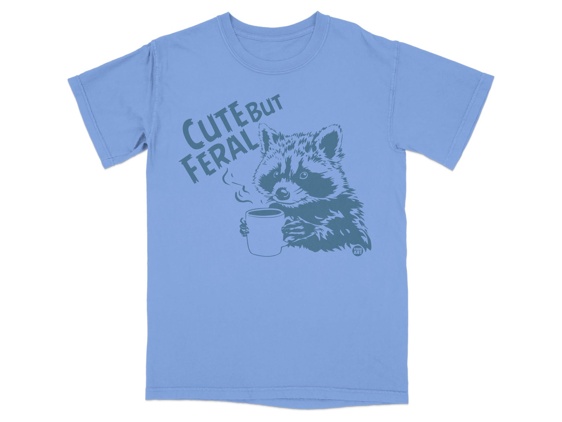 Blue t-shirt with a raccoon holding a steaming mug, reading "CUTE BUT FERAL".