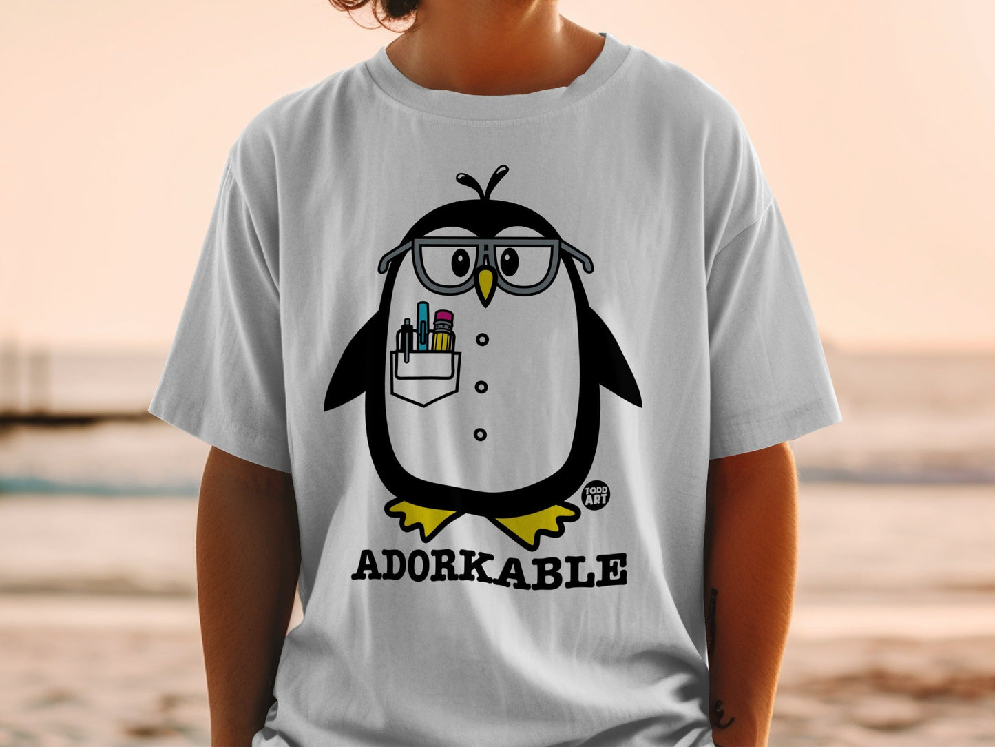 T-shirt with cartoon penguin wearing glasses and holding art supplies.