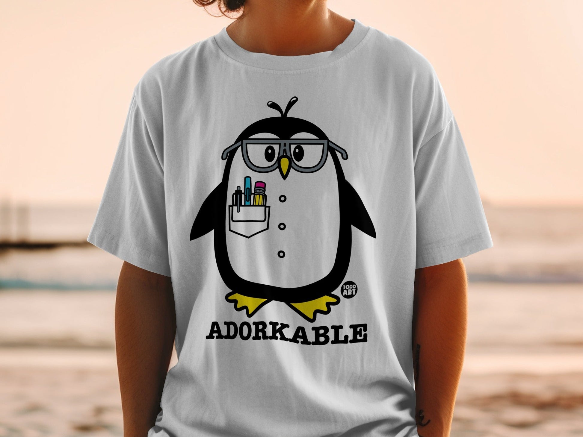 T-shirt with cartoon penguin wearing glasses and holding art supplies.