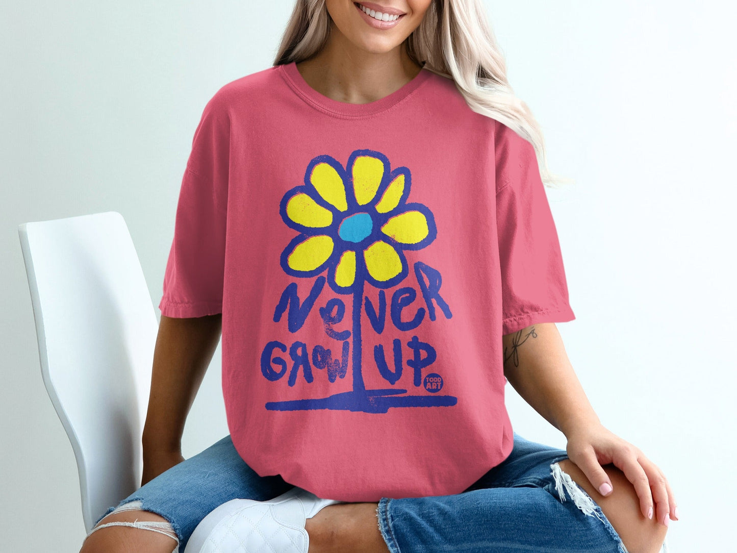 Pink t-shirt with a blue and yellow flower graphic and "Never Grow Up" text.