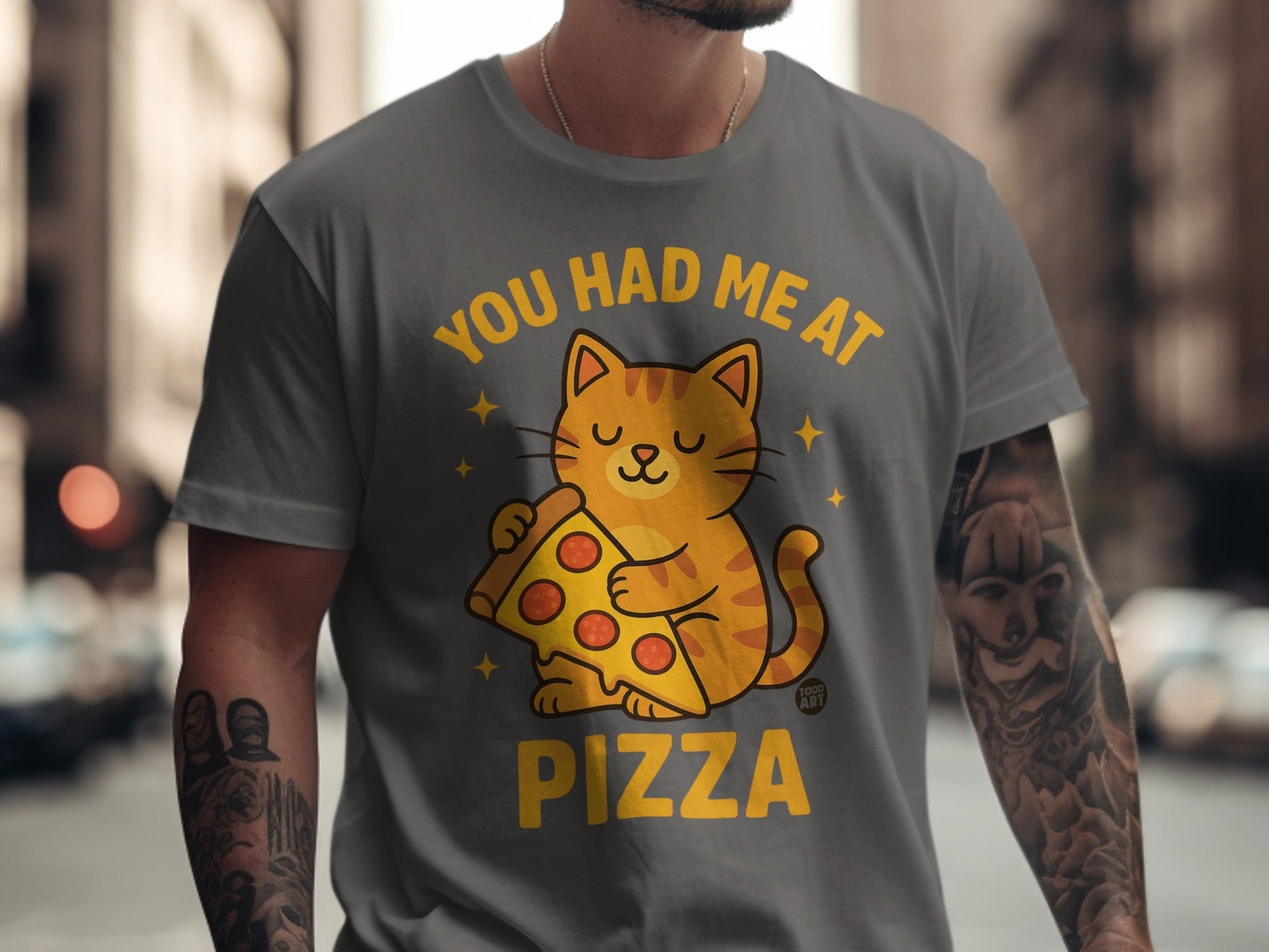 Yellow cat holding pizza slice on grey t-shirt with text "YOU HAD ME AT PIZZA".