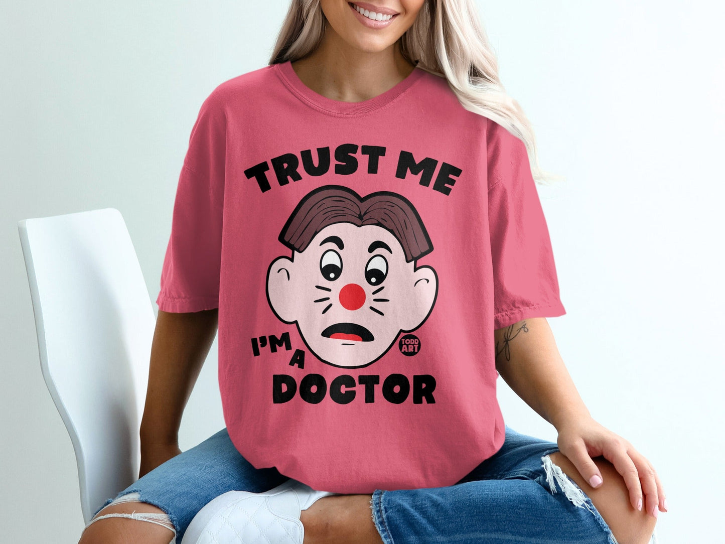 Pink t-shirt with text "TRUST ME I'M A DOCTOR" and a clown face graphic.