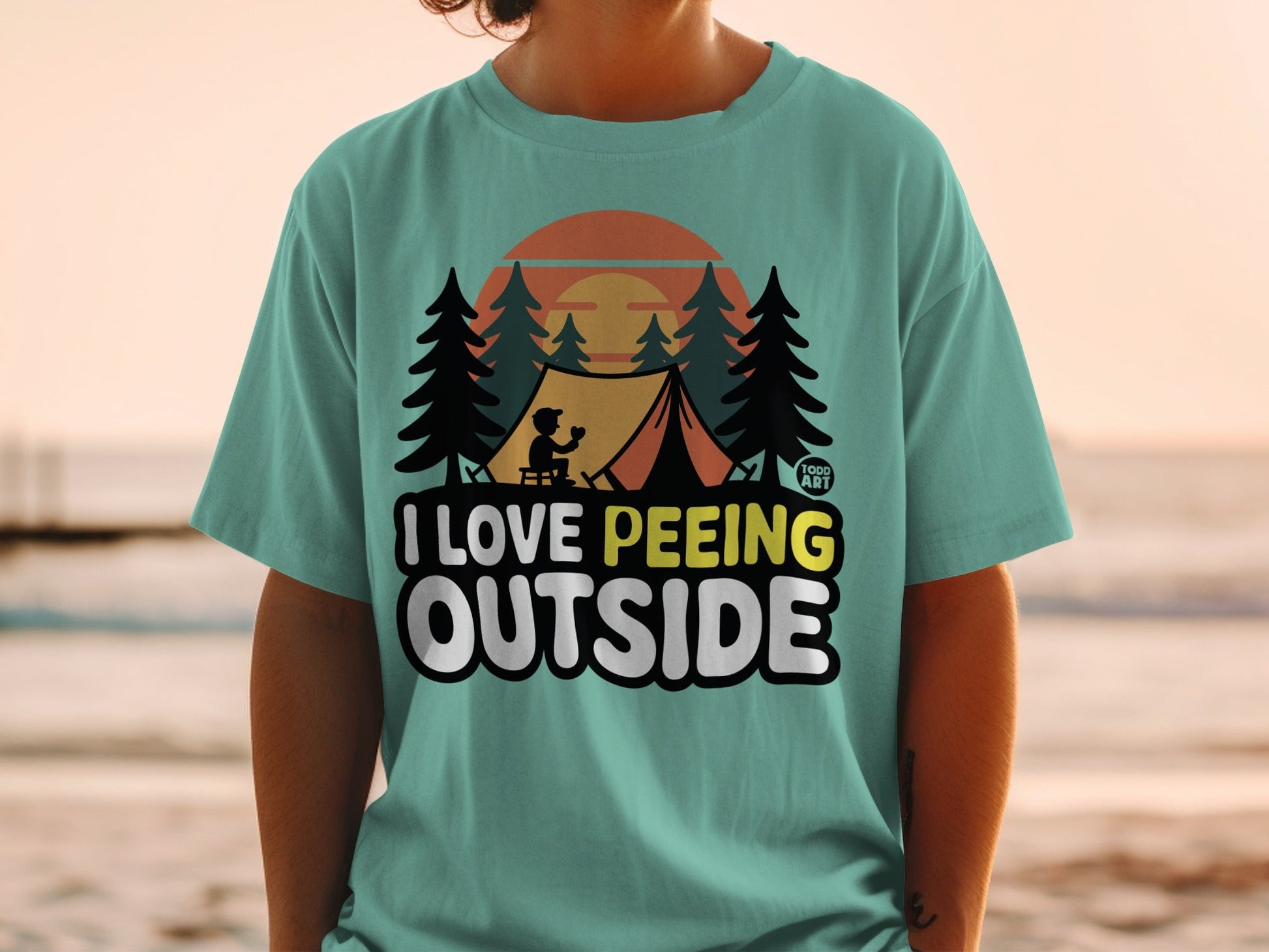 T-shirt with "I Love Peeing Outside" text, camping scene, trees, sunset.