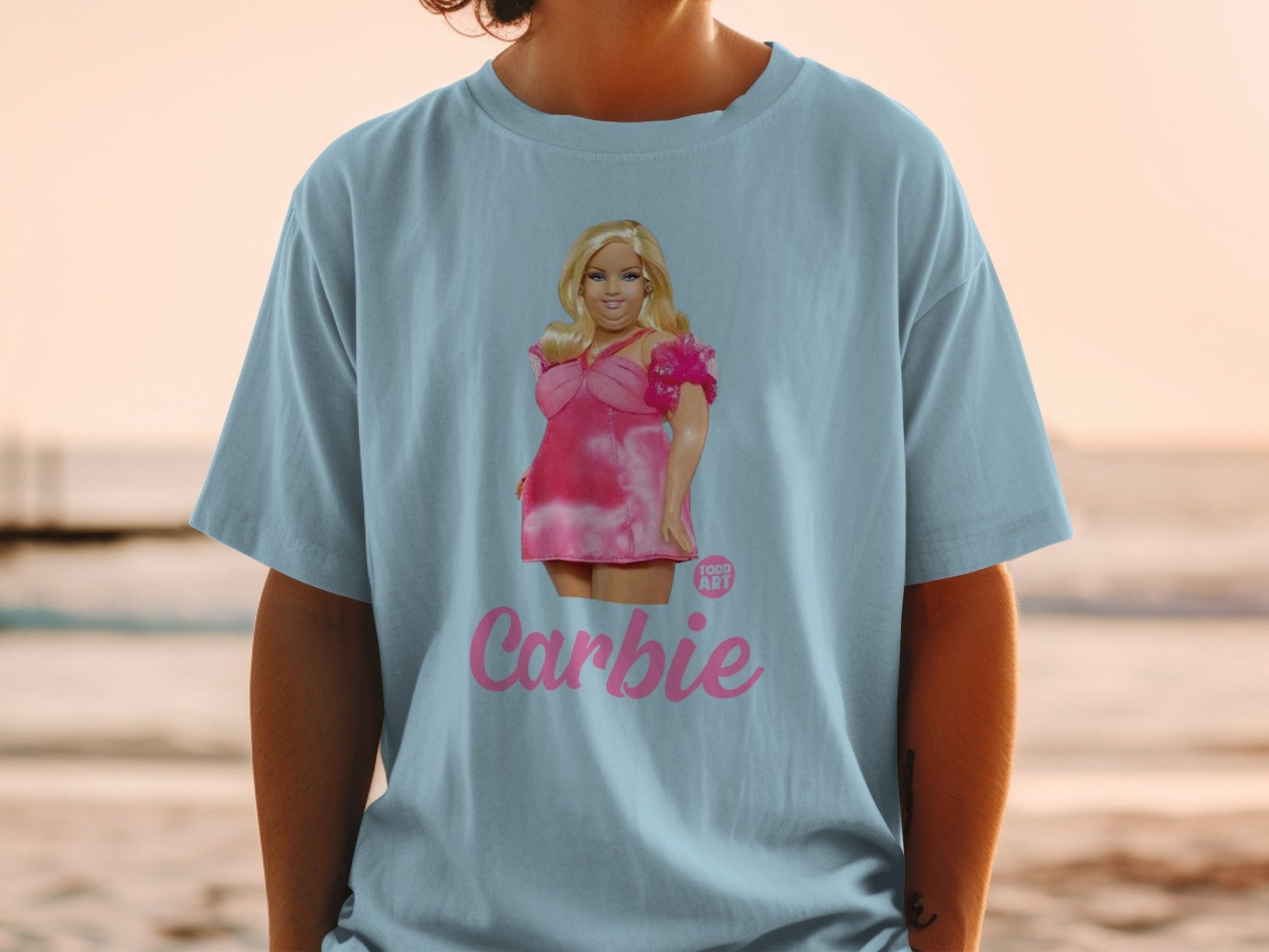 Woman wearing a light blue t-shirt with a pink Barbie graphic and text.