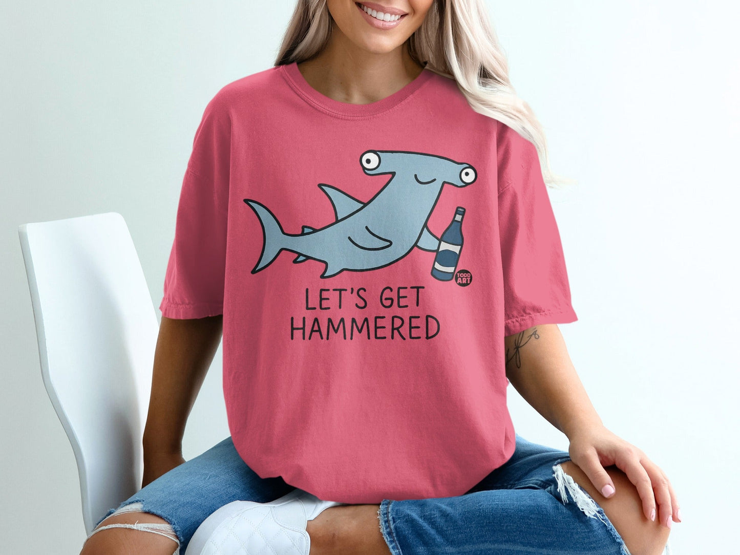 Salmon pink t-shirt with cartoon hammerhead shark holding a bottle.