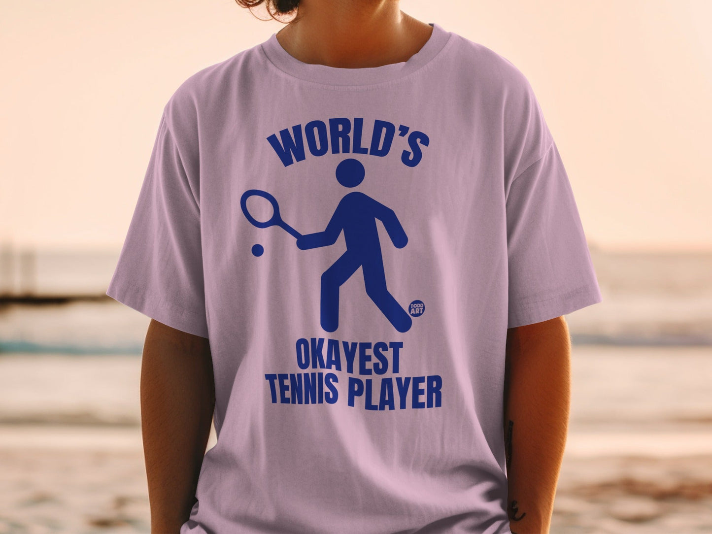 Purple t-shirt with blue graphic of a tennis player and text "WORLD'S OKAYEST TENNIS PLAYER".