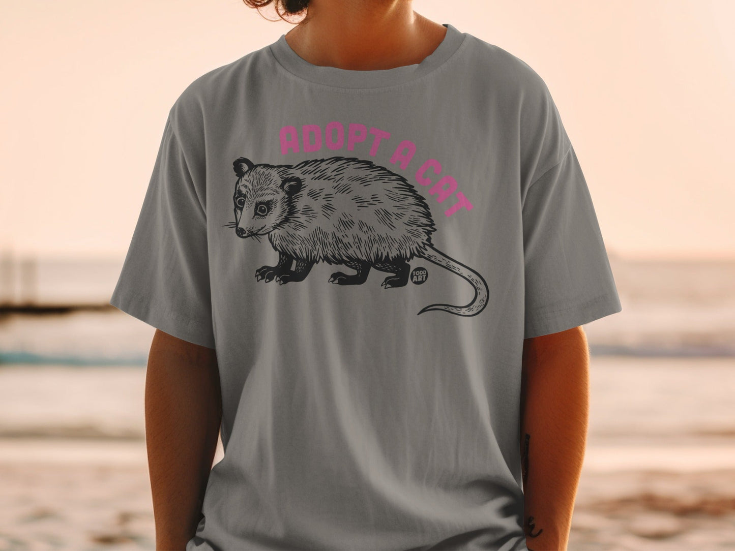 Gray t-shirt with opossum illustration and "ADOPT A CAT" text.