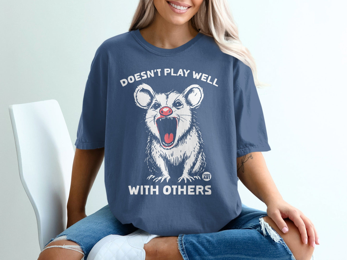 Dark blue t-shirt with a white possum graphic and text reading "Doesn't play well with others."