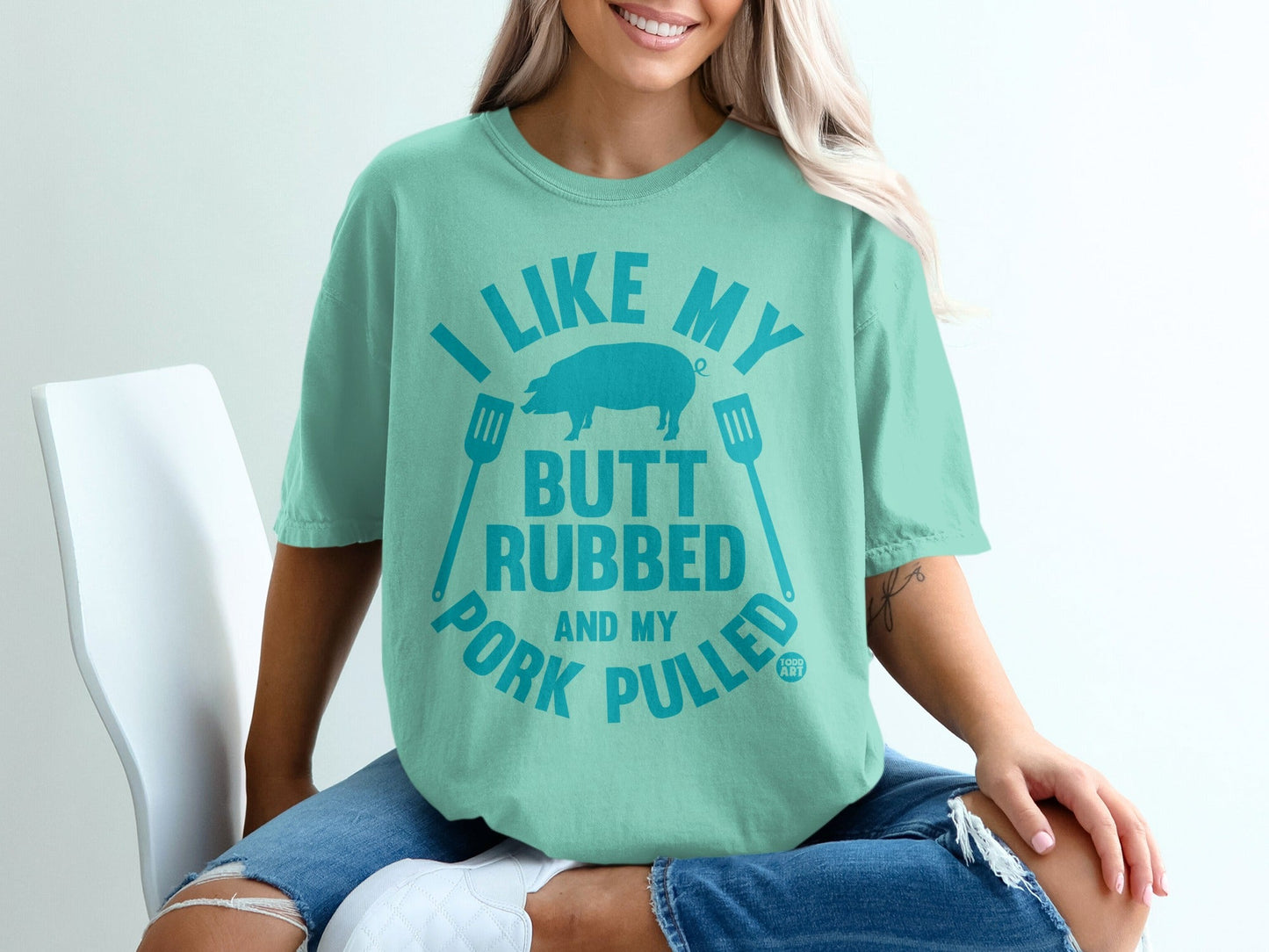 Teal t-shirt with text "I LIKE MY BUTT RUBBED AND MY PORK PULLED" and pig silhouette.