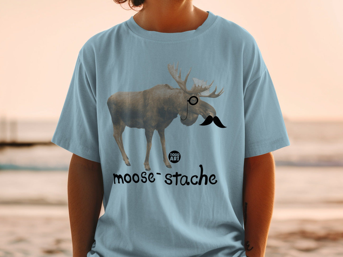 Light blue t-shirt with moose wearing a monocle and mustache.