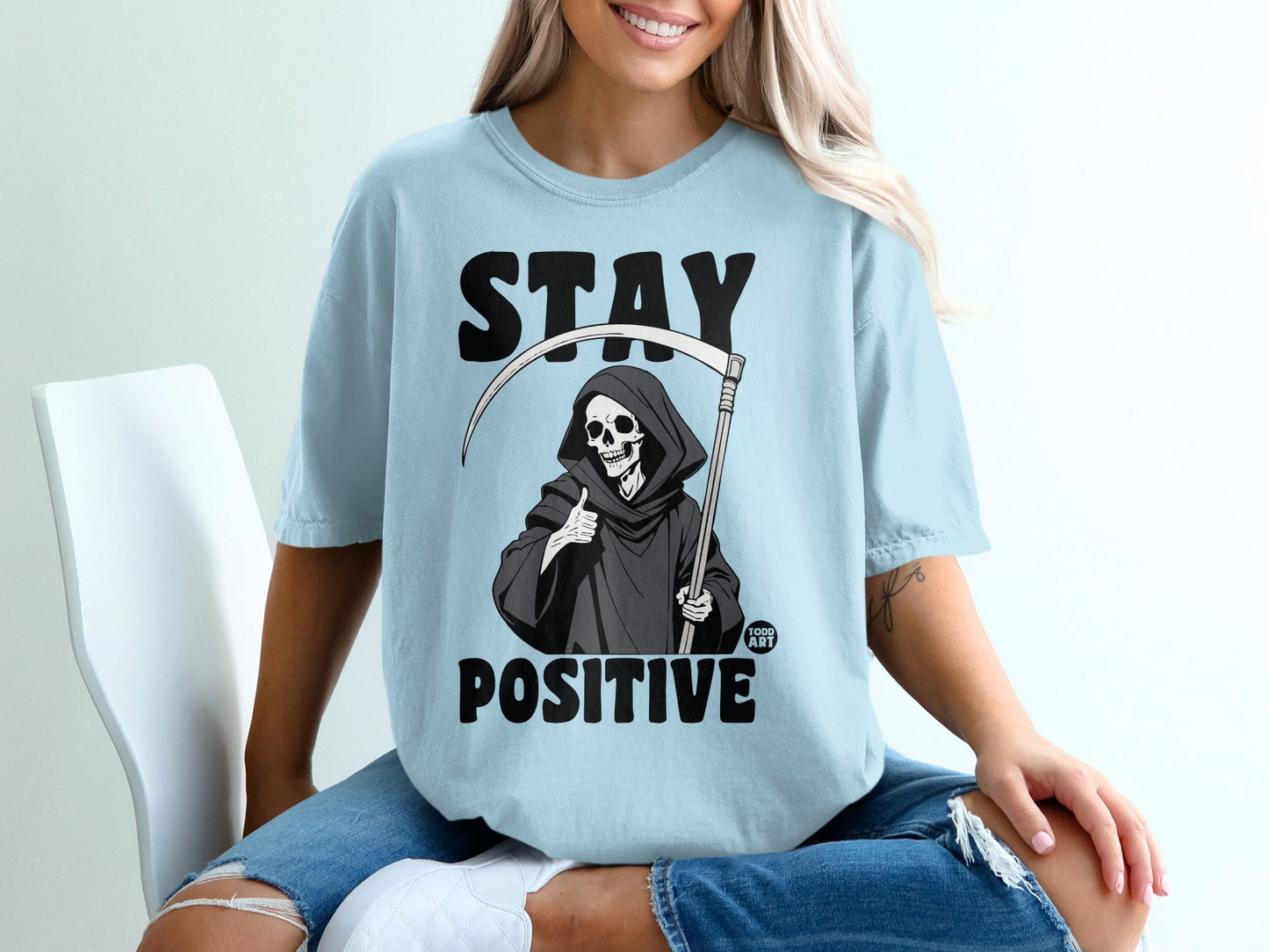 Light blue t-shirt with Grim Reaper giving thumbs up and "STAY POSITIVE" text.