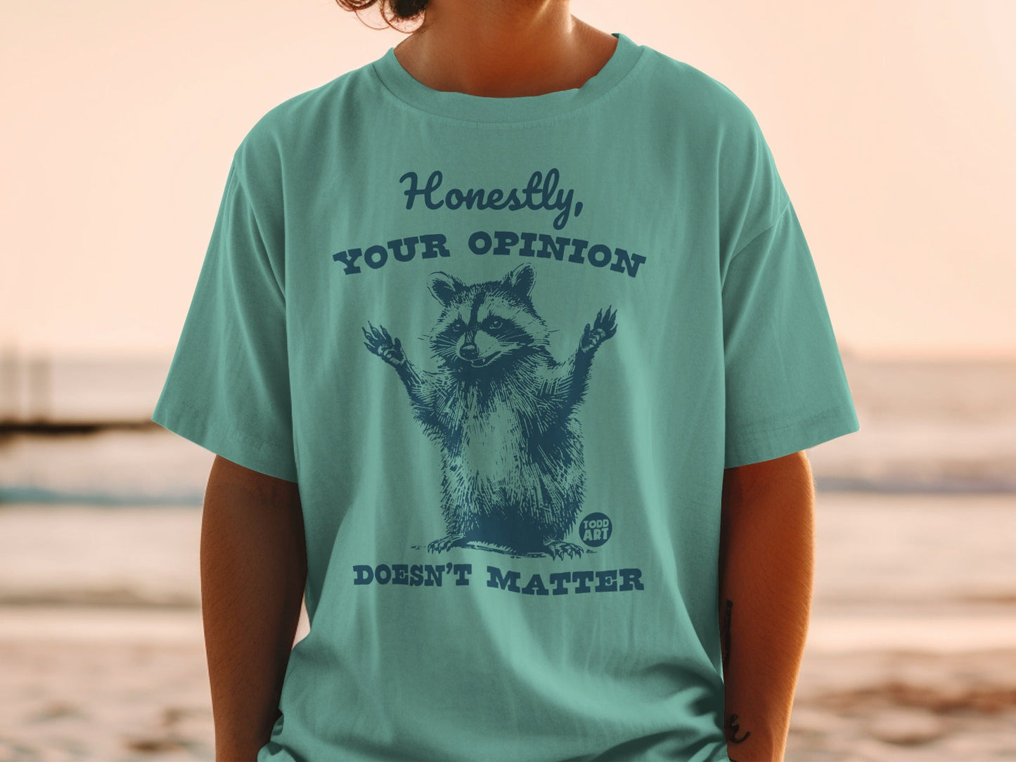 Teal t-shirt with raccoon graphic and text "Honestly, YOUR OPINION DOESN'T MATTER".