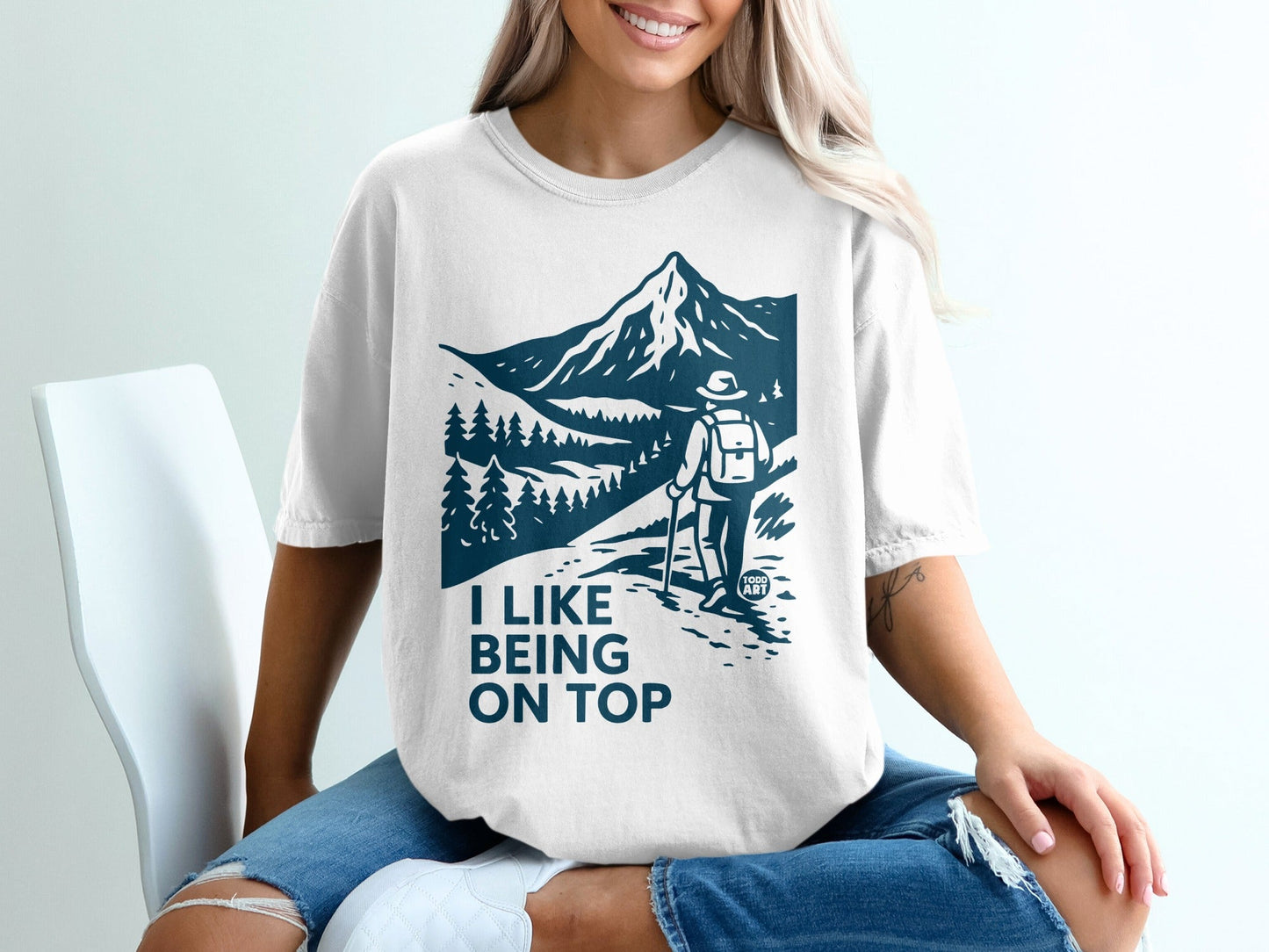 White t-shirt with hiker on mountain path graphic and "I LIKE BEING ON TOP" text.