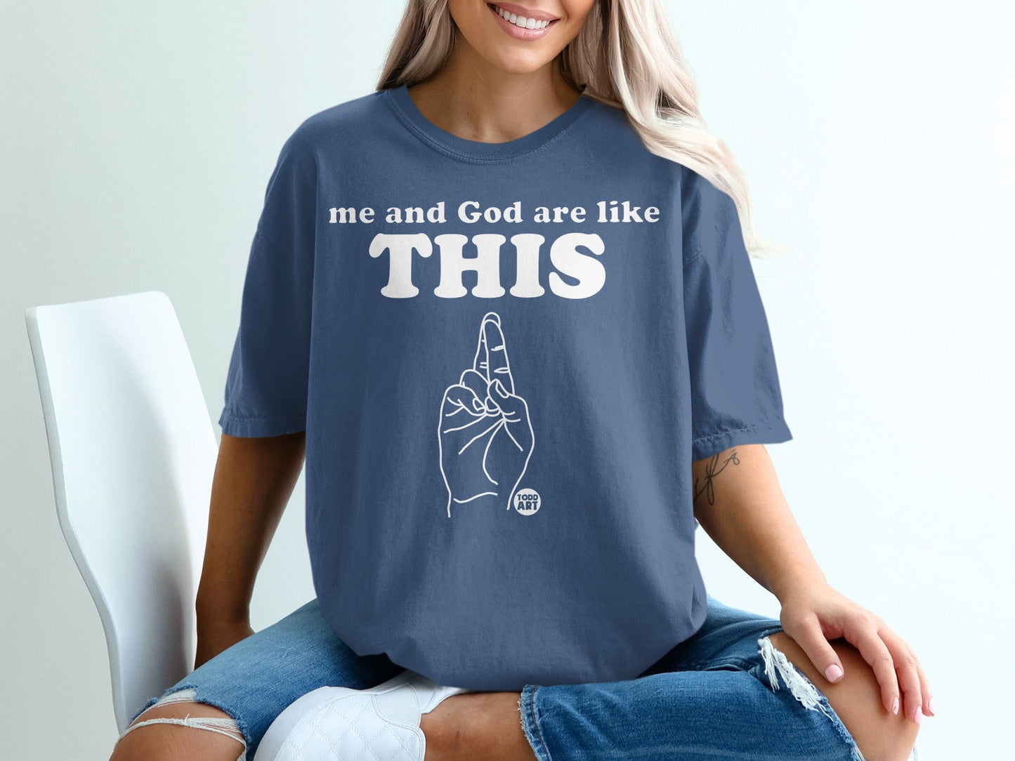 Woman wearing a blue t-shirt with "me and God are like THIS" and a pointing finger graphic.