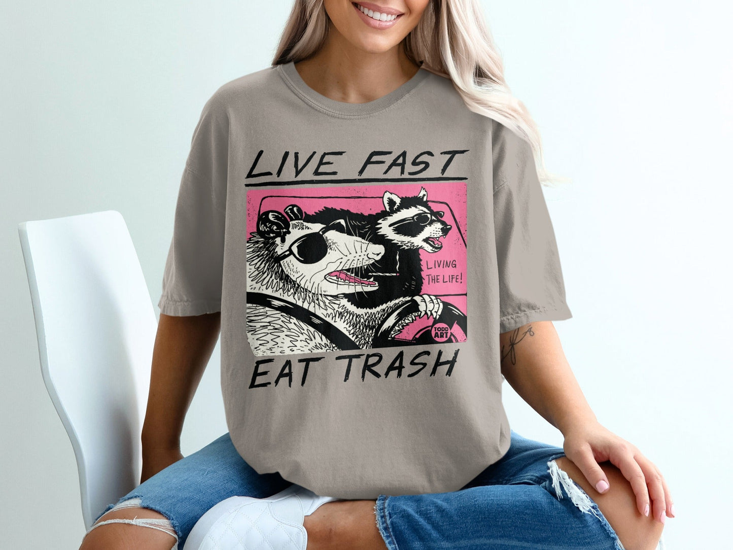 T-shirt with graphic of raccoon and opossum driving, reading "Live Fast, Eat Trash".