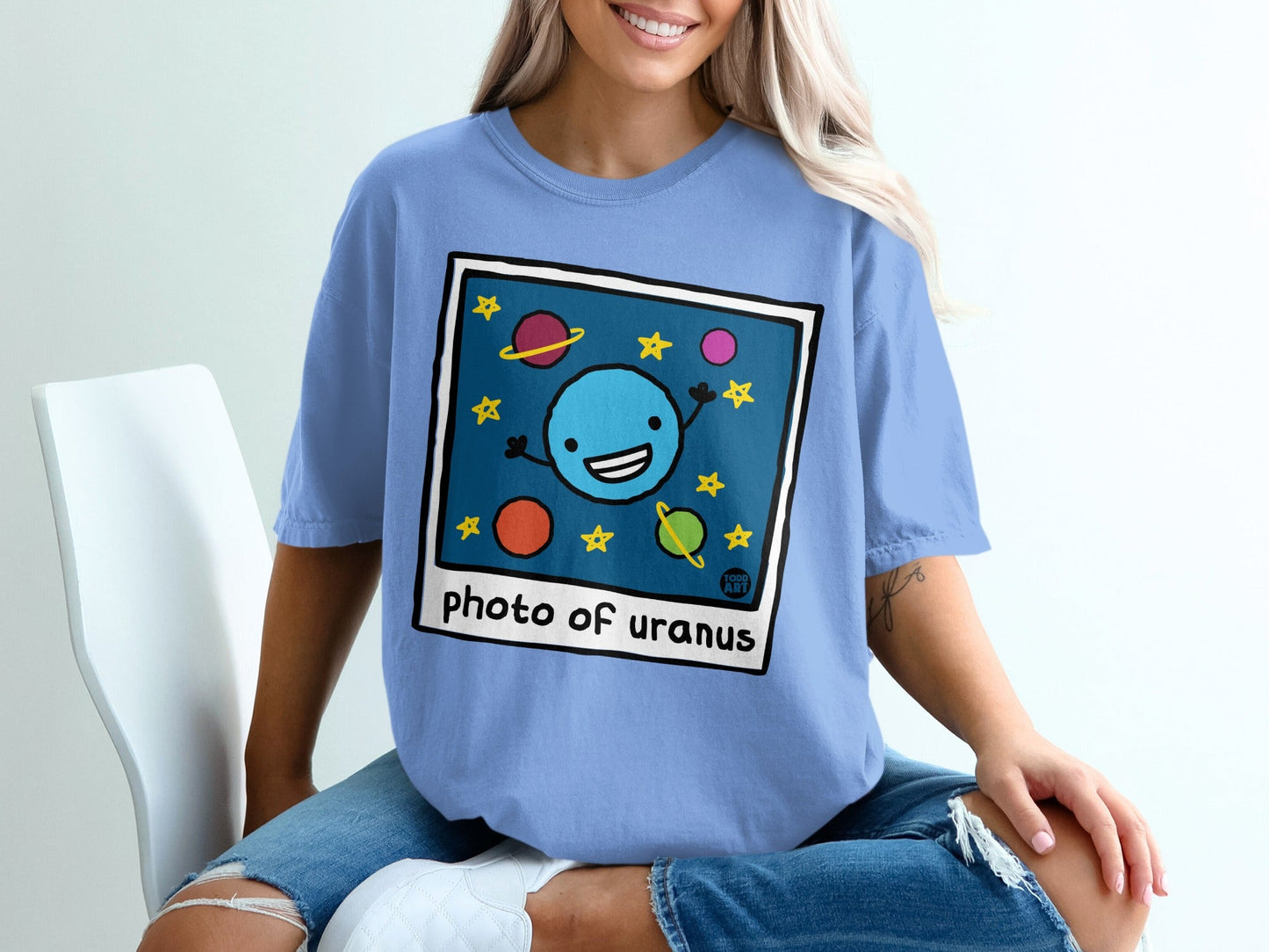 Blue t-shirt with cartoon drawing of a smiling planet Uranus and stars.