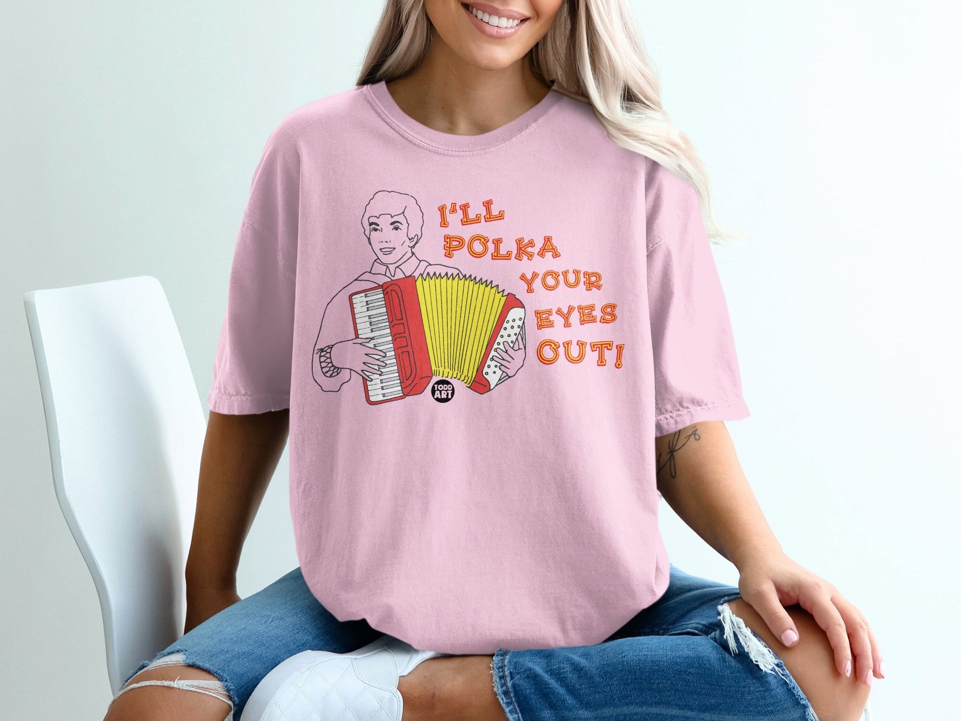 Pink t-shirt with cartoon accordion player and text "I'LL POLKA YOUR EYES OUT!"