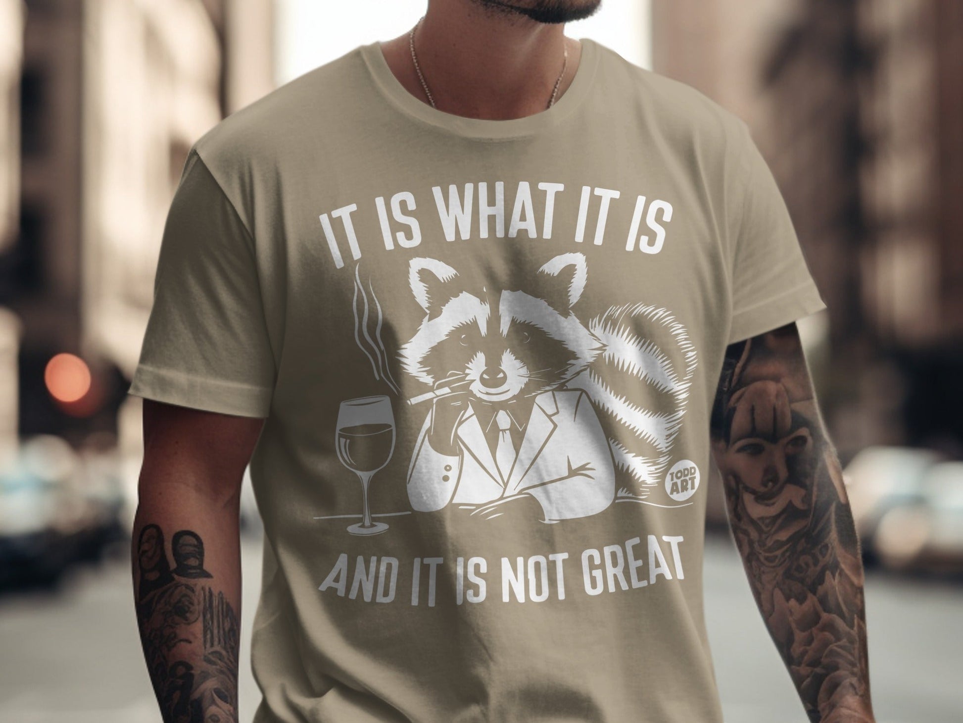 T-shirt with a raccoon in a suit smoking, text reads "IT IS WHAT IT IS AND IT IS NOT GREAT".