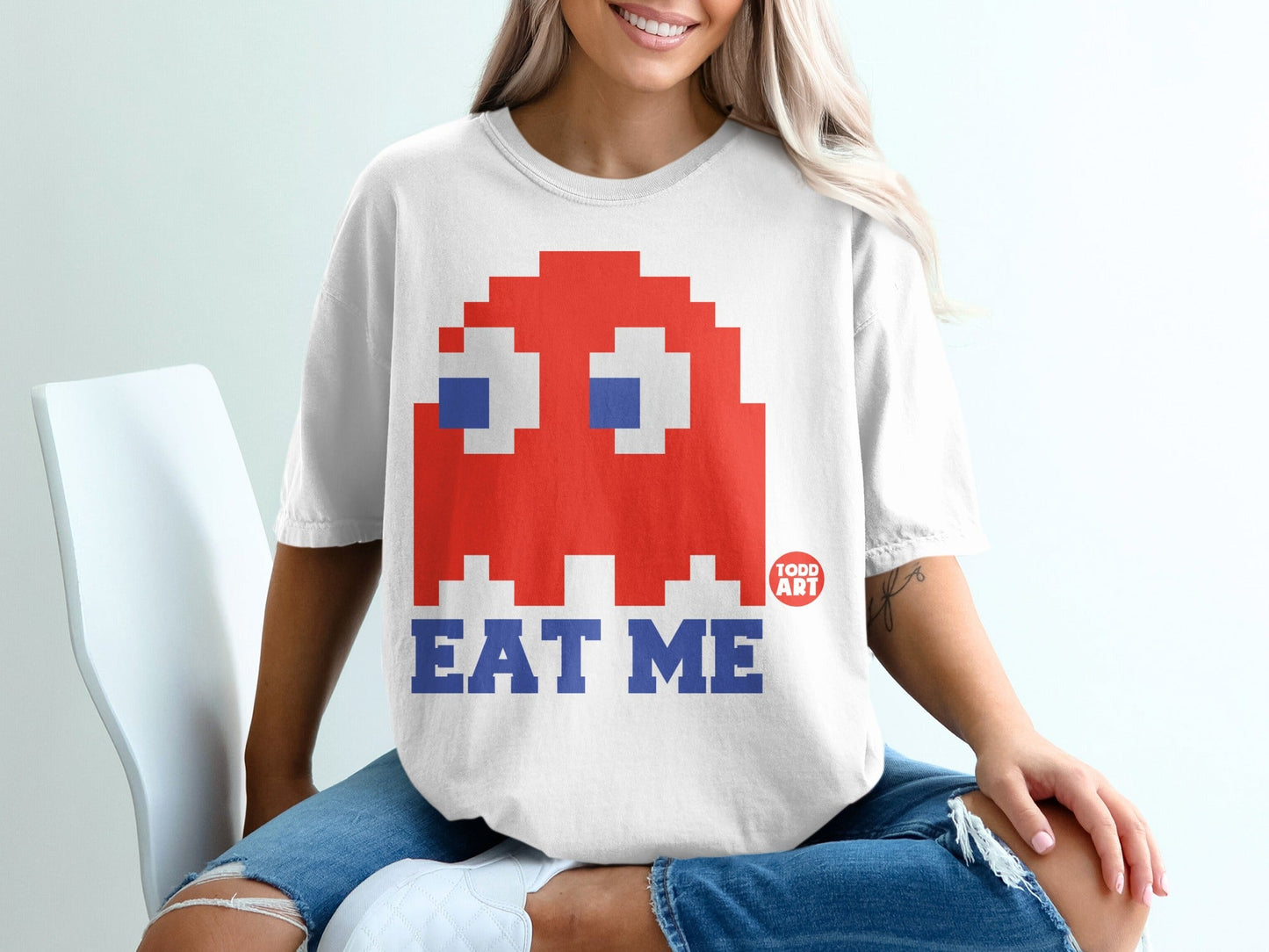 White t-shirt with red Pac-Man ghost and "EAT ME" text.