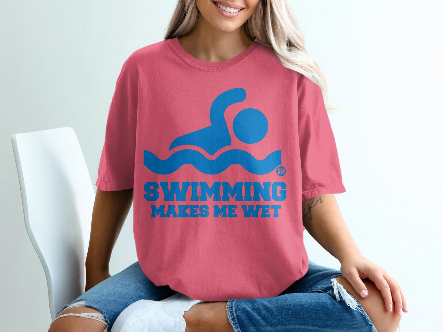Coral t-shirt with blue "SWIMMING MAKES ME WET" text and swimmer graphic.