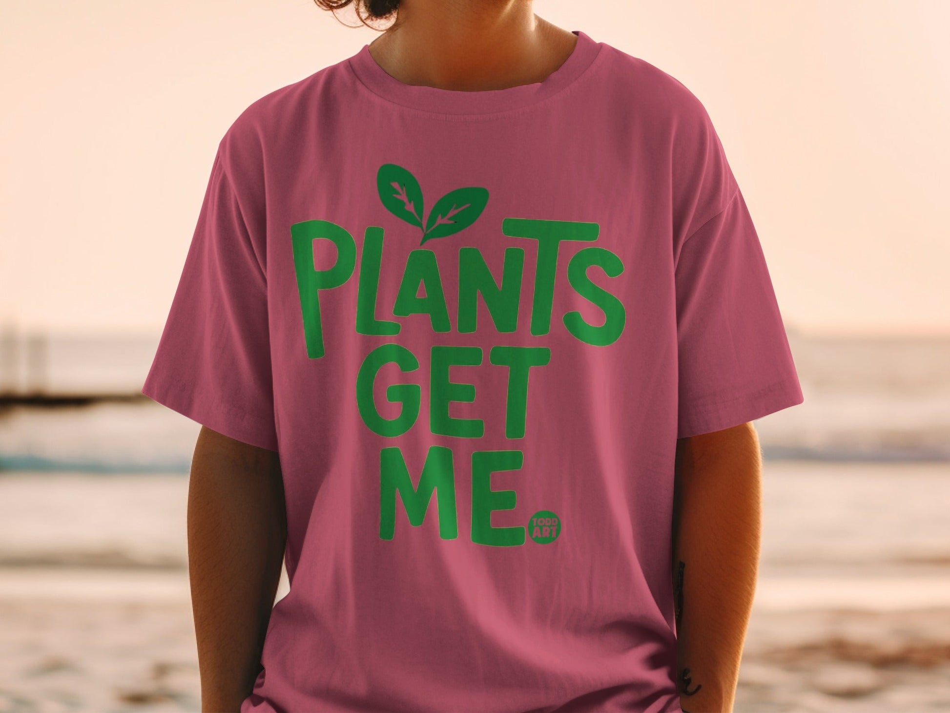 Pink t-shirt with green text "PLANTS GET ME" and small plant logo.