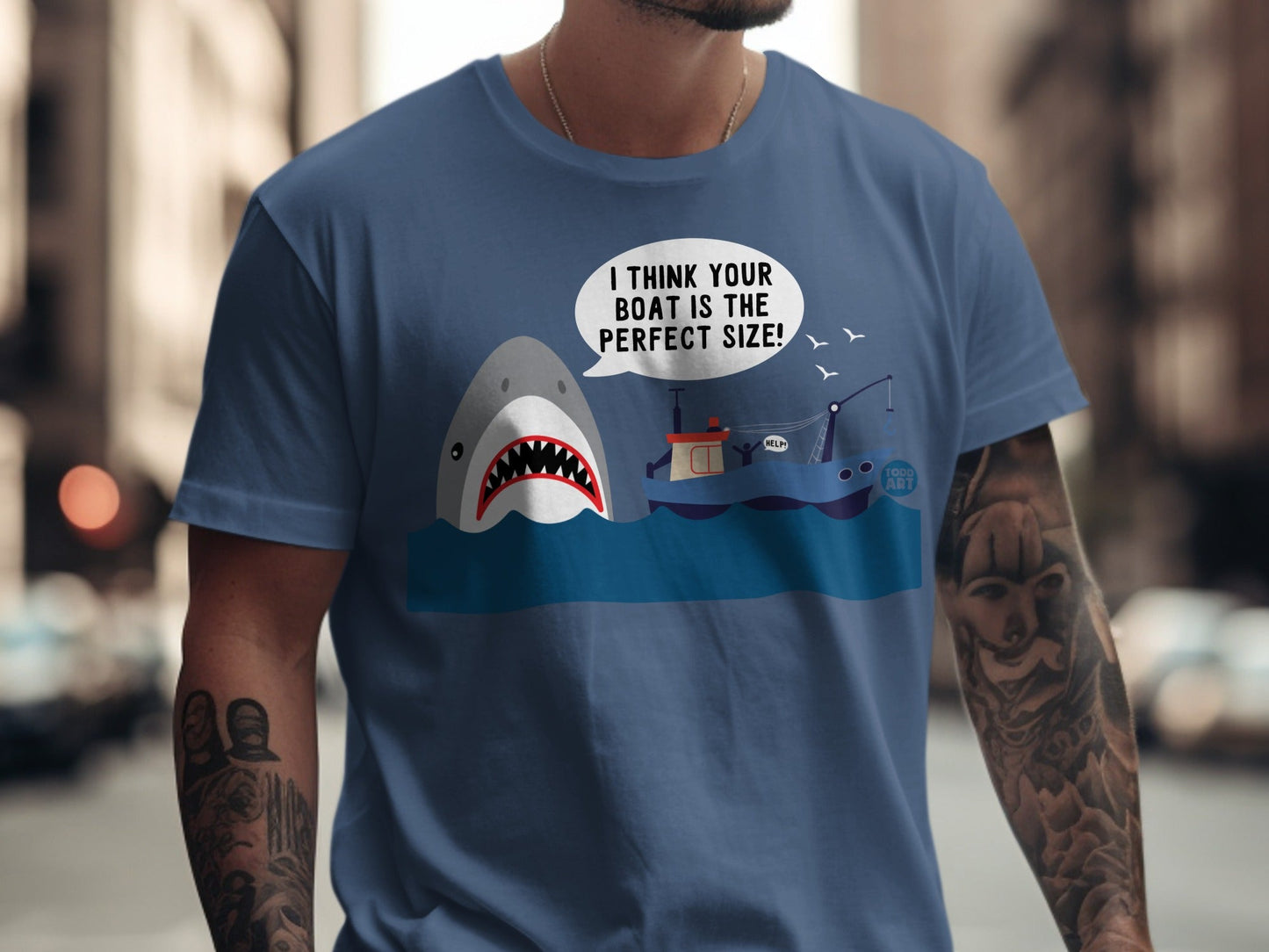 T-shirt graphic of a shark attacking a small boat with text "I THINK YOUR BOAT IS THE PERFECT SIZE!".
