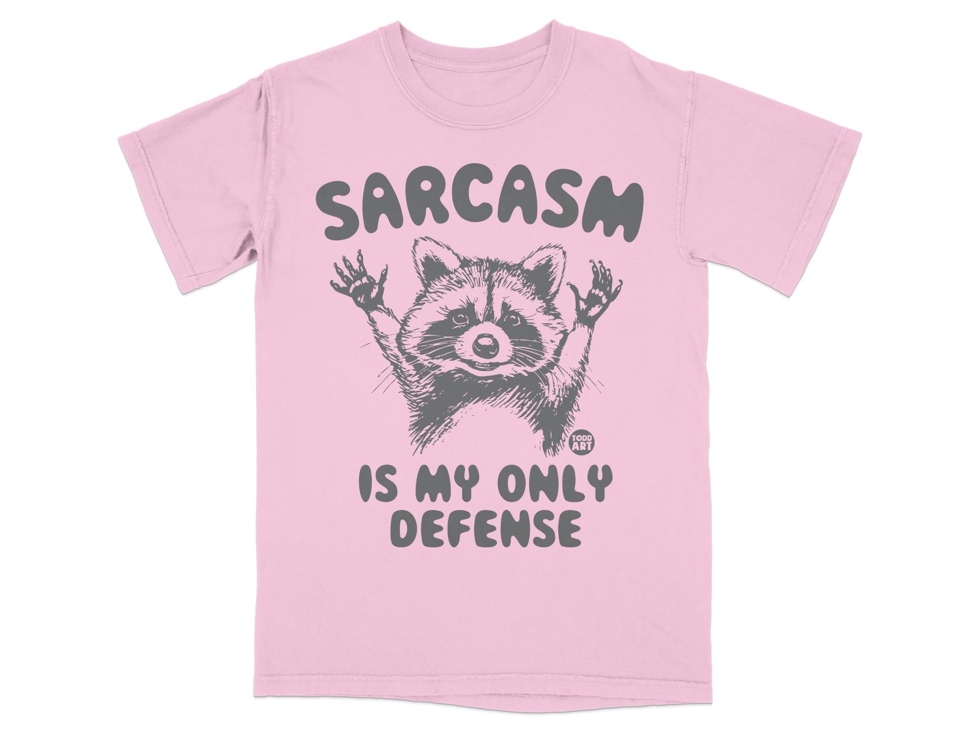 Pink t-shirt with raccoon graphic and text "SARCASM IS MY ONLY DEFENSE".