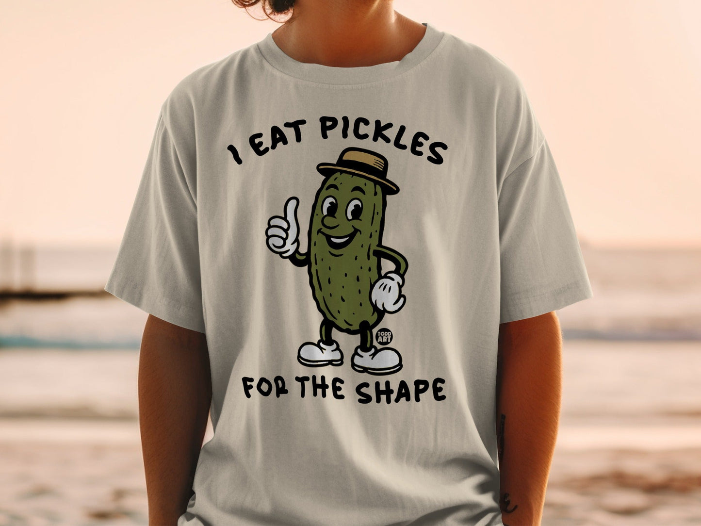 T-shirt with cartoon pickle wearing hat giving thumbs up, text "I EAT PICKLES FOR THE SHAPE".