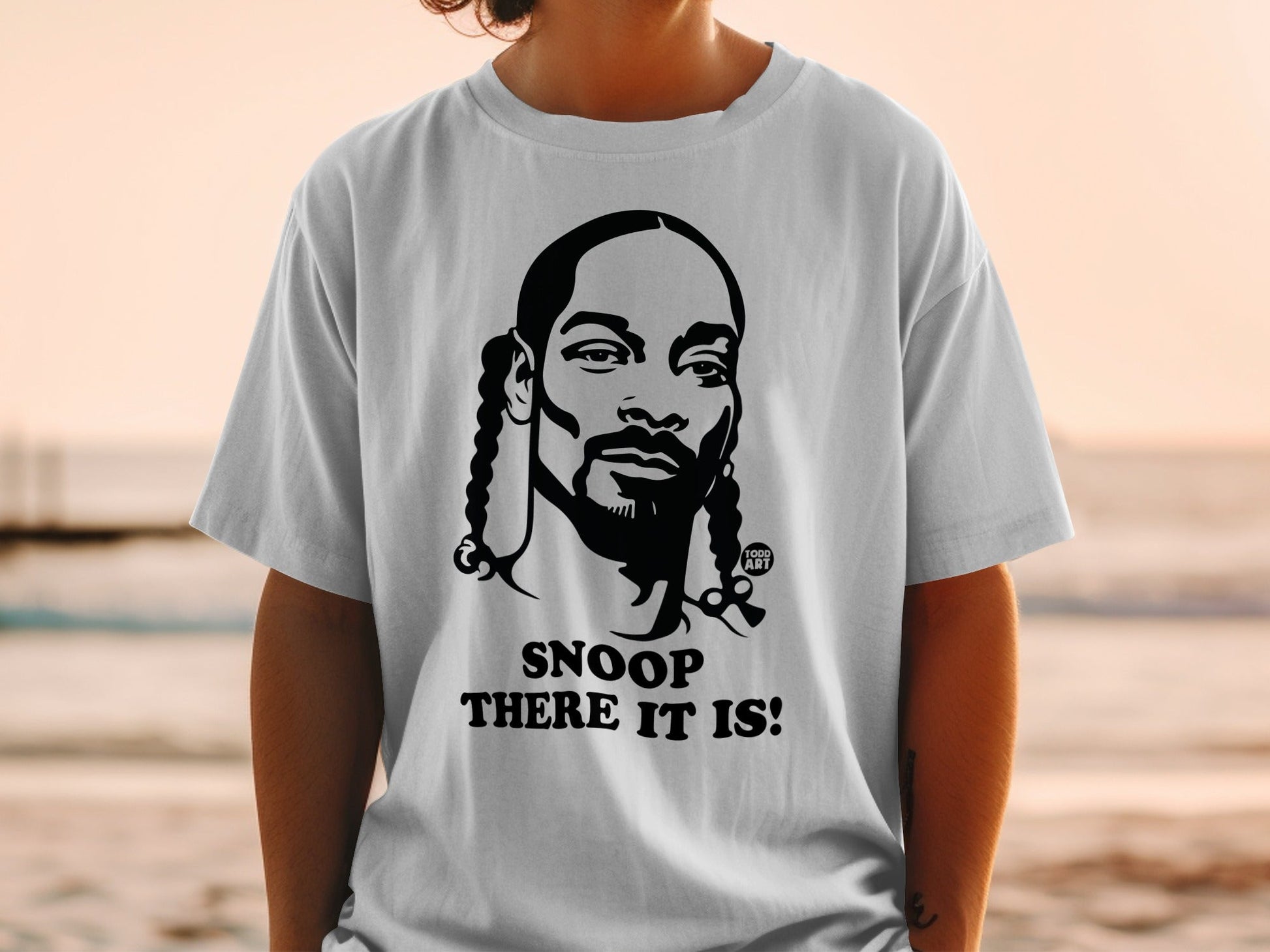 White t-shirt with black graphic of Snoop Dogg's face and text "Snoop There It Is!".