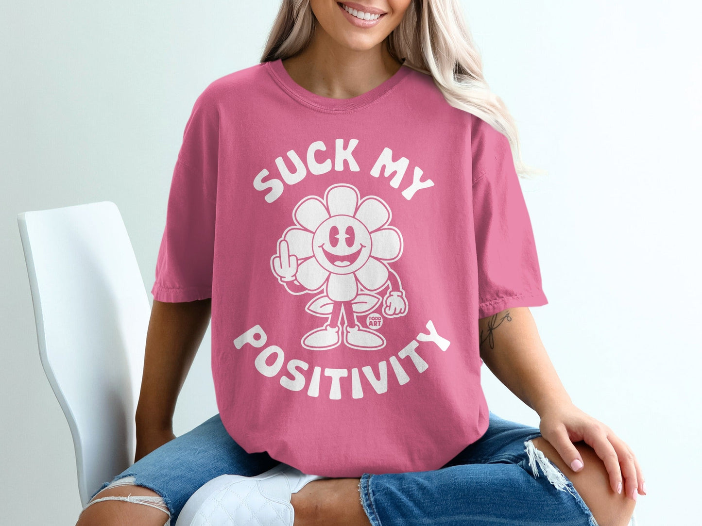 Pink t-shirt with graphic of a smiling flower giving the middle finger and text "SUCK MY POSITIVITY".