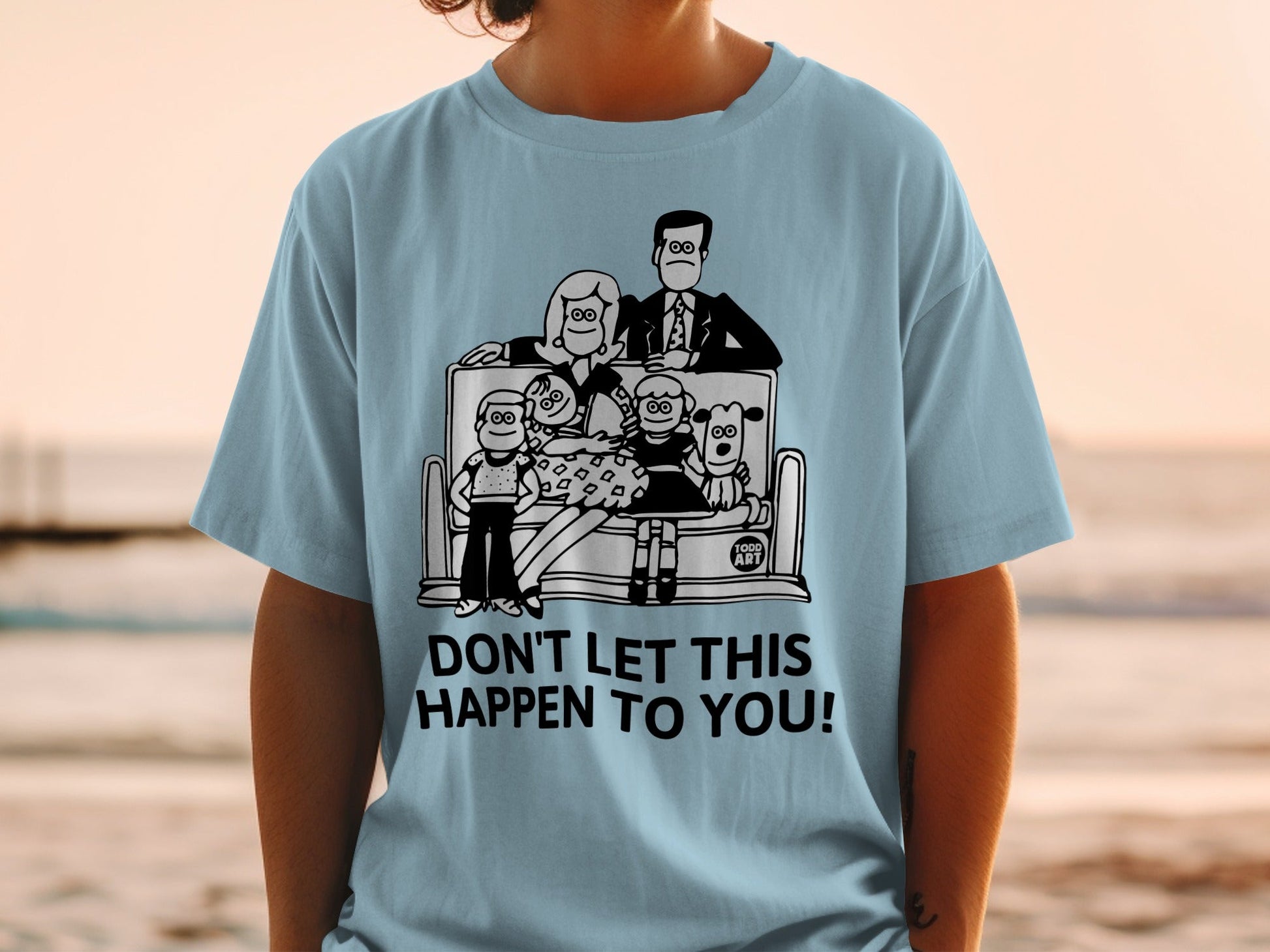 Light blue t-shirt with cartoon family and dog on a bench.