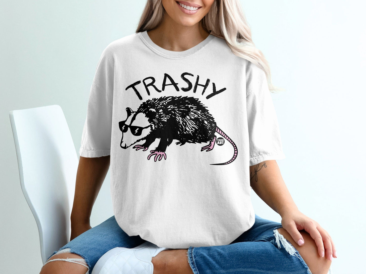 White t-shirt with "TRASHY" text and a cartoon opossum wearing sunglasses.
