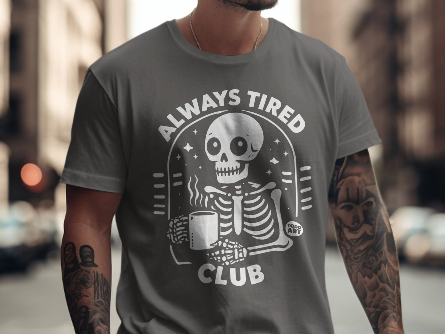 Gray t-shirt with white skeleton holding coffee mug and "ALWAYS TIRED CLUB" text.
