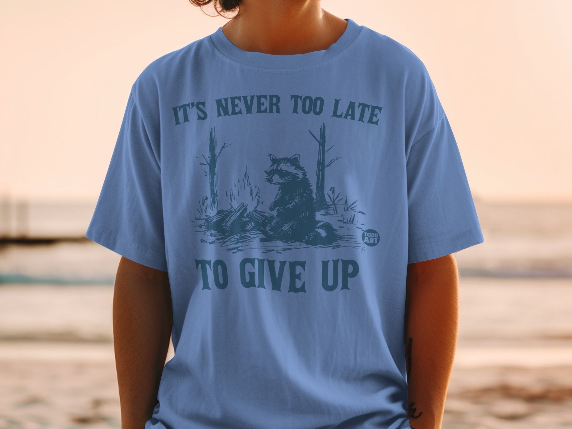 T-shirt with raccoon illustration and text "IT'S NEVER TOO LATE TO GIVE UP".