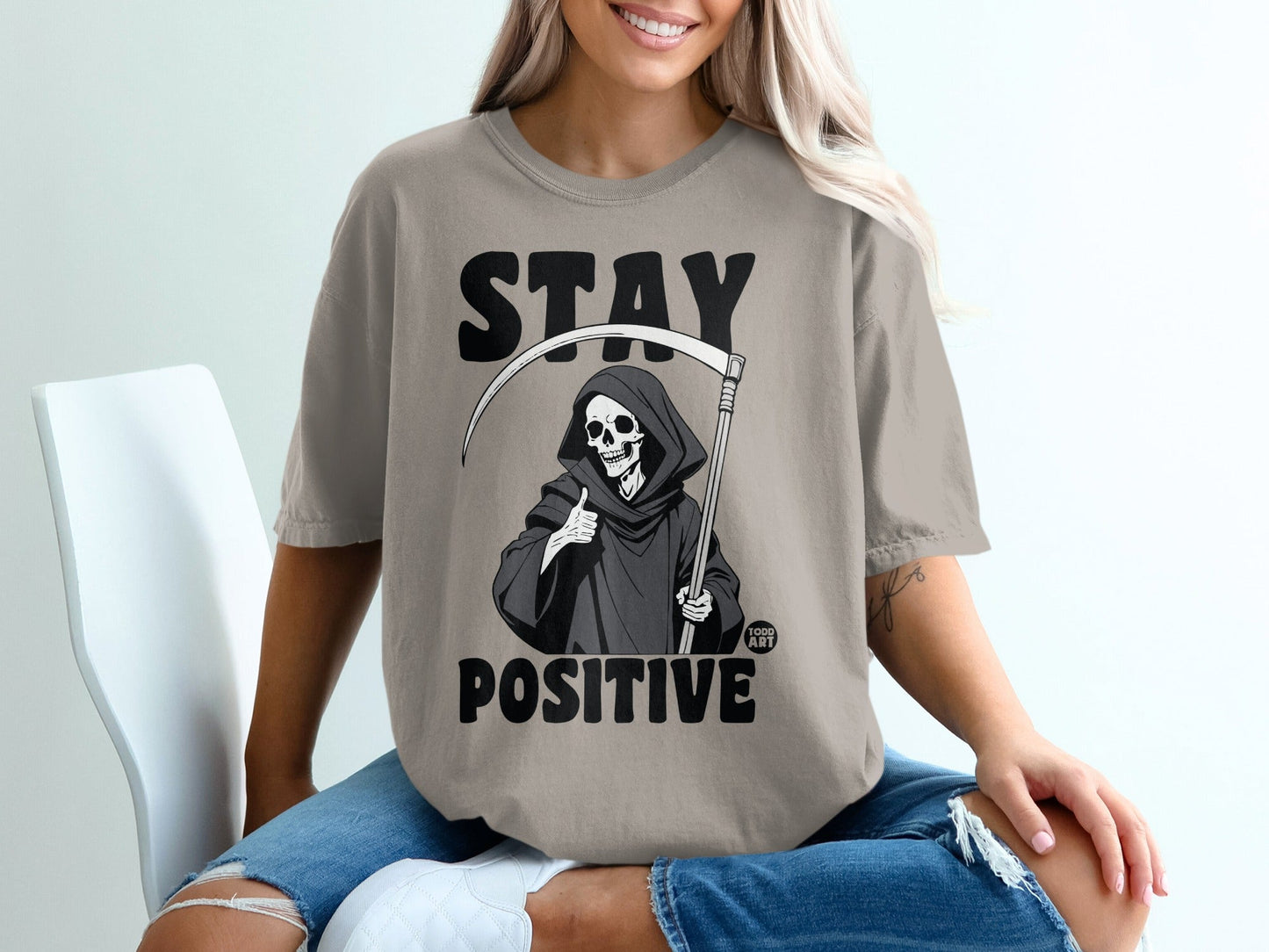 Grim Reaper with scythe and thumbs up on a t-shirt reading "STAY POSITIVE".