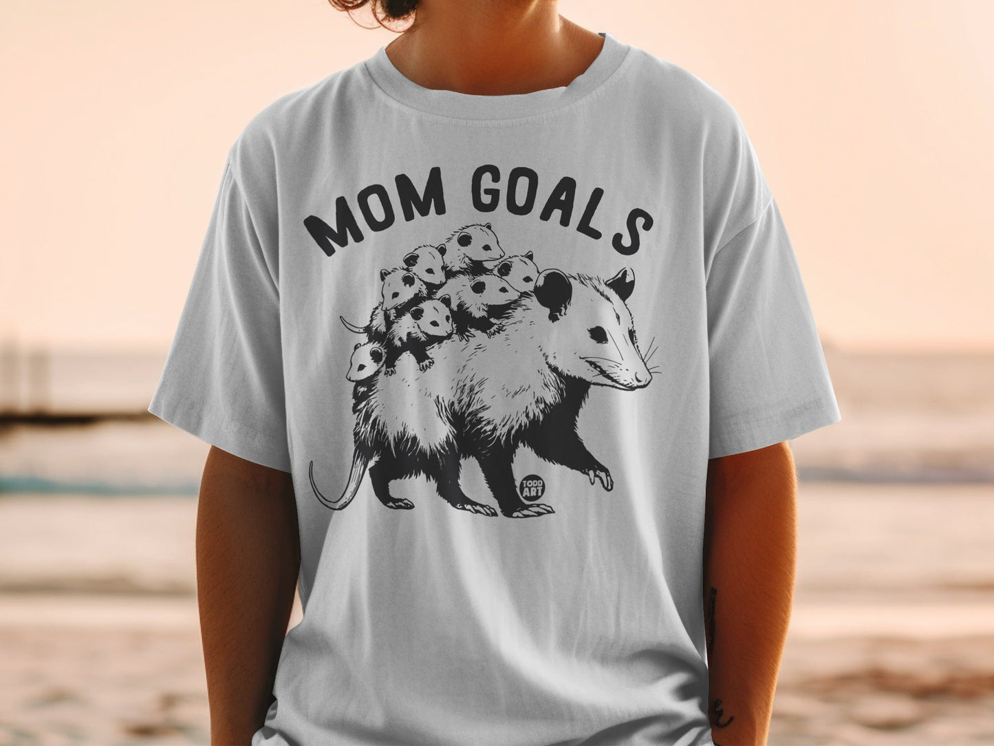 T-shirt graphic of a mother possum with babies on her back, text "Mom Goals".