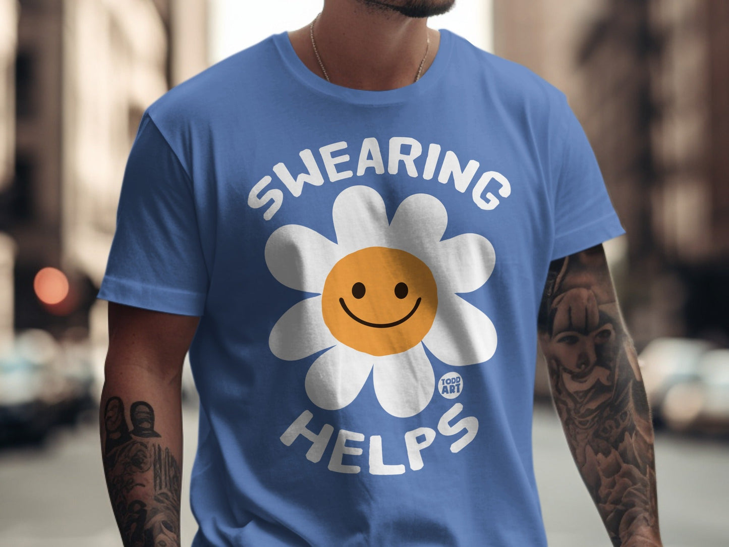 Blue t-shirt with white text "SWEARING HELPS" and a smiling daisy.