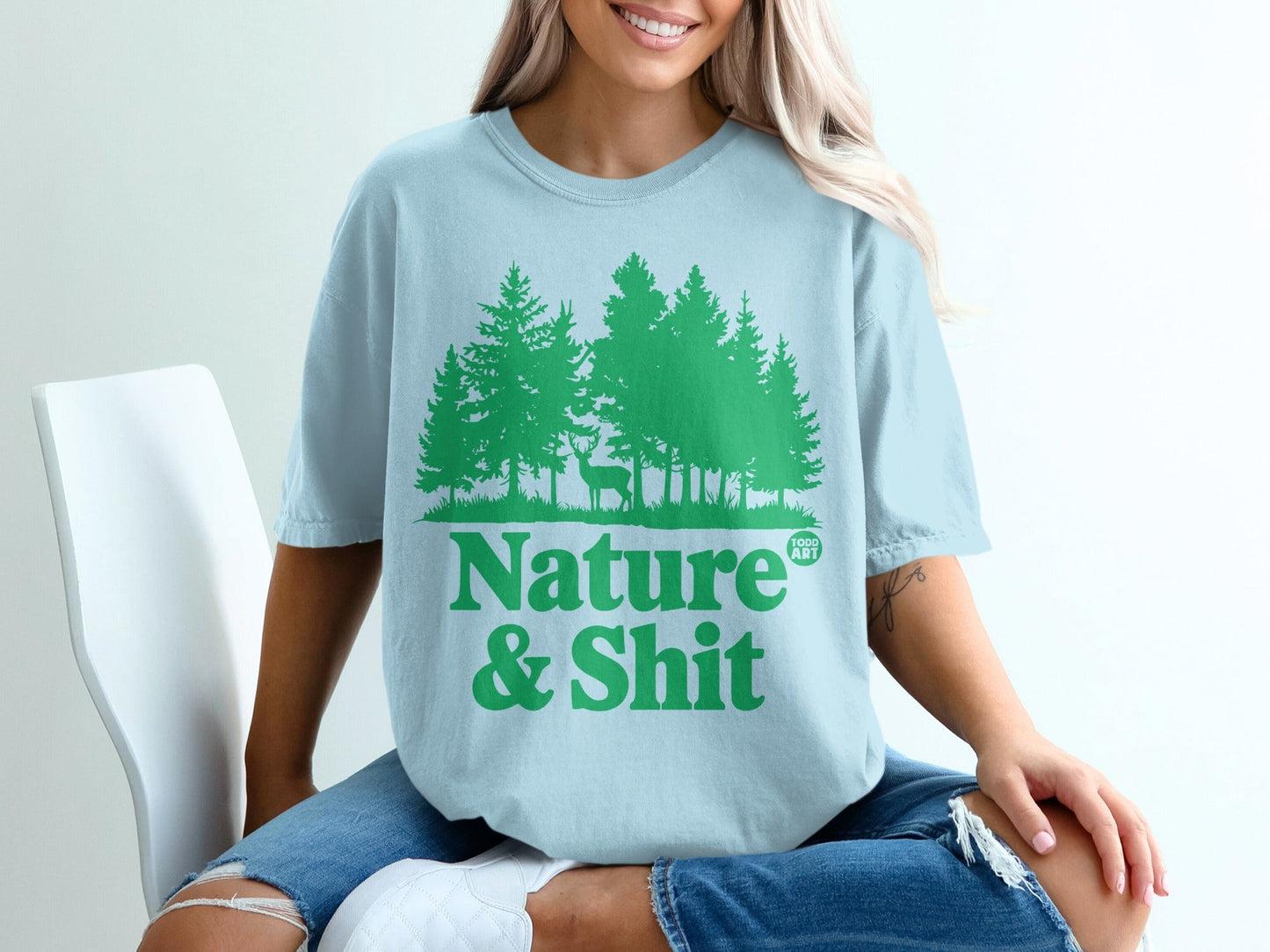 Light blue t-shirt with green pine trees and deer, text reads "Nature & Shit".