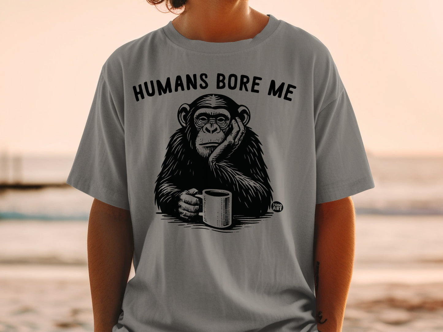 T-shirt with black and white graphic of chimpanzee holding coffee cup, text "HUMANS BORE ME".