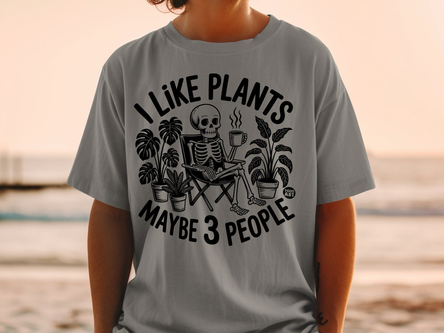 T-shirt with skeleton surrounded by plants, holding coffee, text reads "I like plants, maybe 3 people."