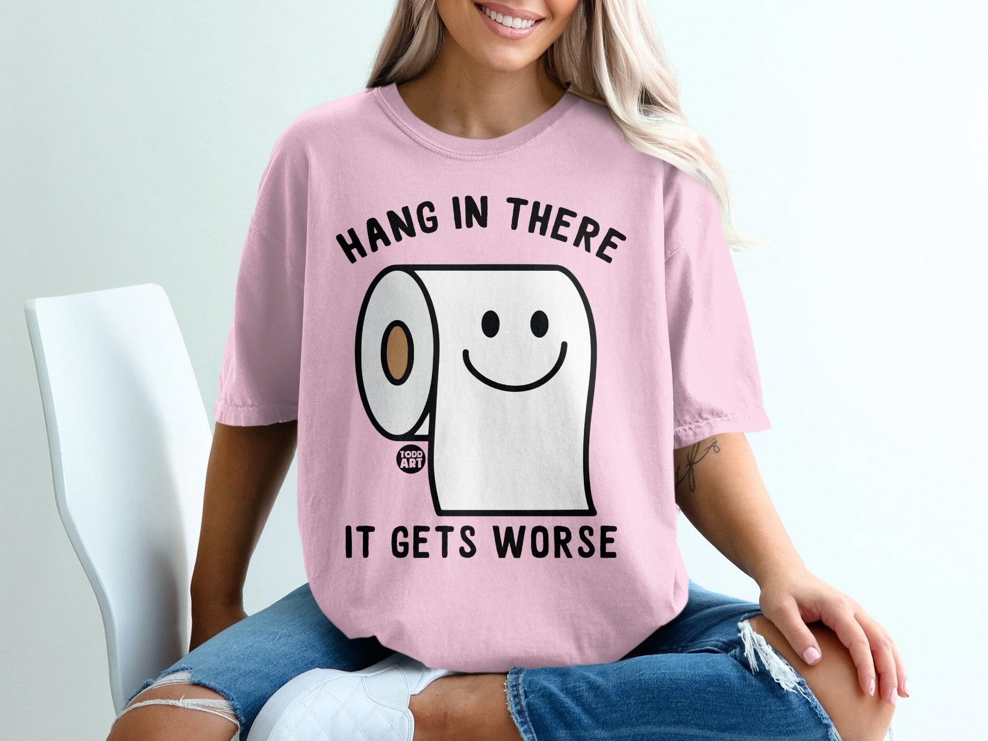 Pink t-shirt with toilet paper graphic and text "Hang in there, it gets worse."