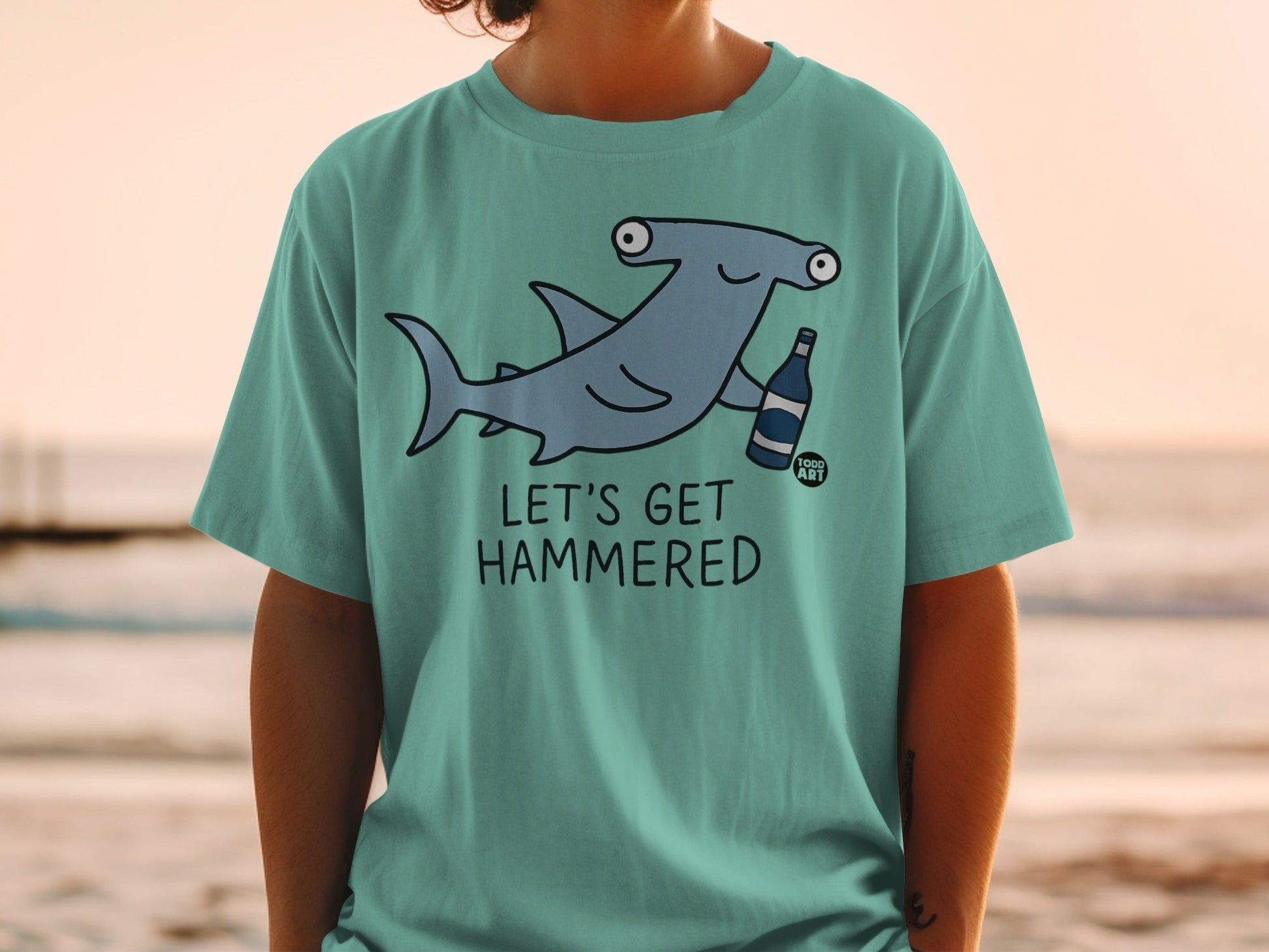 T-shirt with cartoon hammerhead shark holding a bottle, text "LET'S GET HAMMERED".