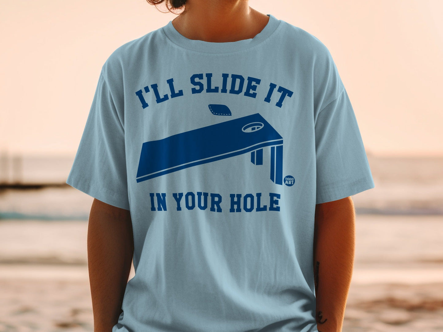 Light blue t-shirt with dark blue text and cornhole board graphic.
