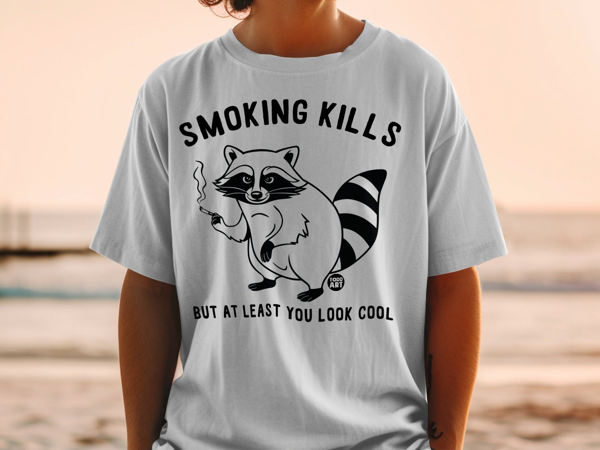 T-shirt with cartoon raccoon smoking and text "SMOKING KILLS BUT AT LEAST YOU LOOK COOL".