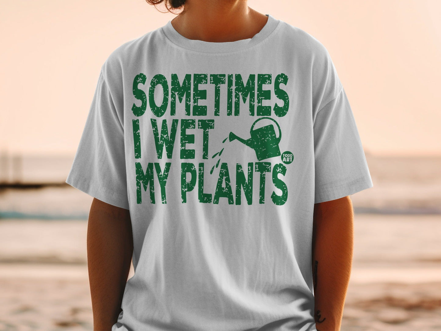 White t-shirt with green text that reads "SOMETIMES I WET MY PLANTS".